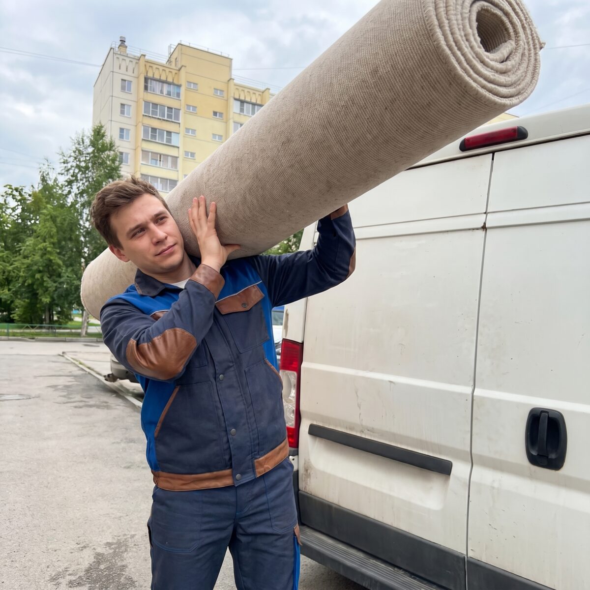 Курьер с рулоном ковра возле автомобиля